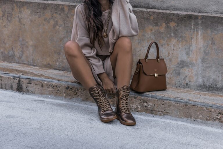 woman sitting on brown concrete surface wearing brown boots beside brown leather handbag